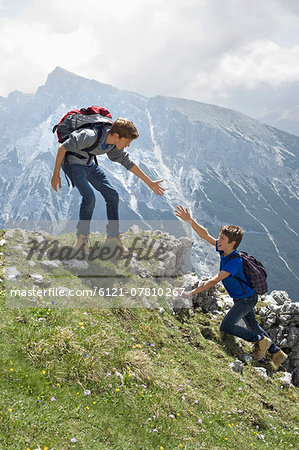 Teenage boys helping friend climbing in mountains