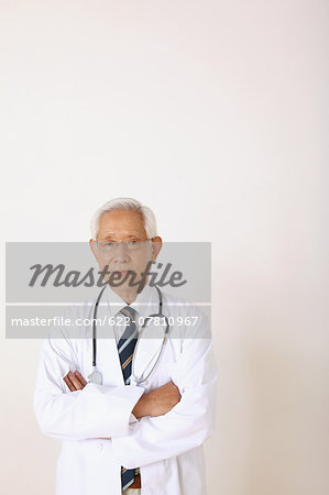 Senior adult Japanese doctor against white wall