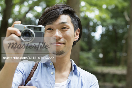 A man in a Kyoto park holding a camera, taking a picture.