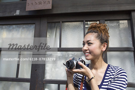 Woman standing outdoors, holding a camera.