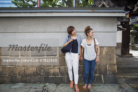 Two women standing outdoors, leaning against a wall.