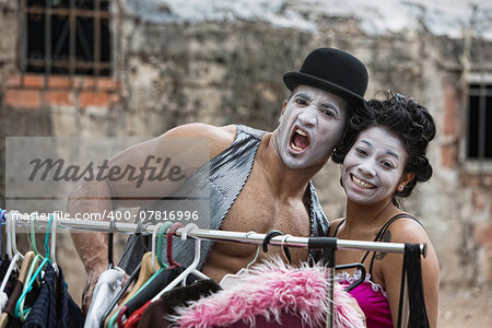 Laughing cirque clowns with makeup at clothing rack