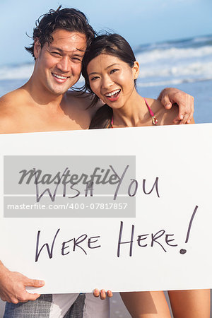Man & woman Asian couple, boyfriend and girlfriend in bikini, on vacation beach holding Wish You Were Here sign