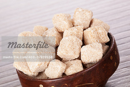 Brown sugar cubes detail in wooden round bowl on brown background. Culinary sugar background in brown.