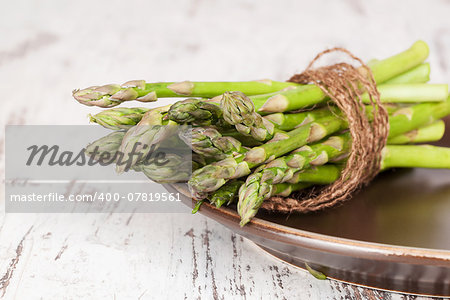 Fresh asparagus bundle on brown plate on white wooden textured background. Culinary healthy vegetable eating.