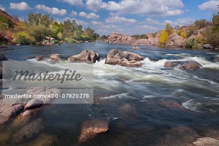 Beautiful sunny Autumn Day on The River with waterfall and big rocks, flowing water