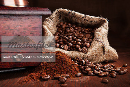 Roasted coffee beans in sack, with old vintage coffee grinder with ground coffee on wooden background. Traditional dark brown coffee still life.