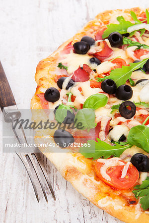 Delicious colorful pizza with tomatoes, melted cheese, black olives, onions, ham and fresh herbs on white wooden background. Culinary mediterranean pizza eating.