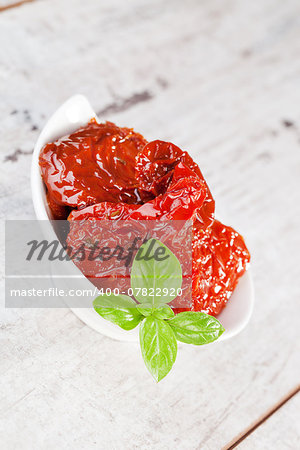 Delicious dried tomatoes with fresh basil leaves in bowl on white textured wooden background. Culinary eating