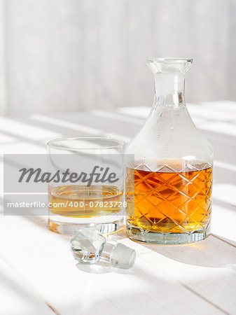 Photo of a whisky decanter and rocks glass on a table by a window.