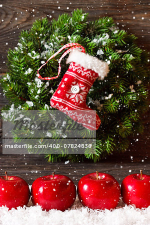 Christmas decoration with hanging wreath and stocking and ripe red apples on snow.