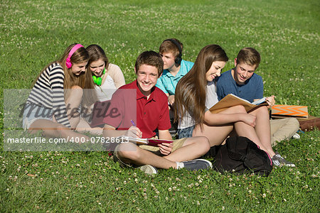 Happy male teenager studying with friends outdoors