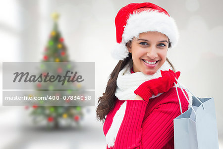 Festive brunette holding shopping bag against blurry christmas tree in room