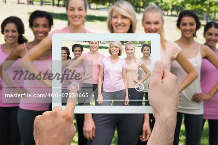 Composite image of hand holding tablet pc showing photograph of breast cancer activists