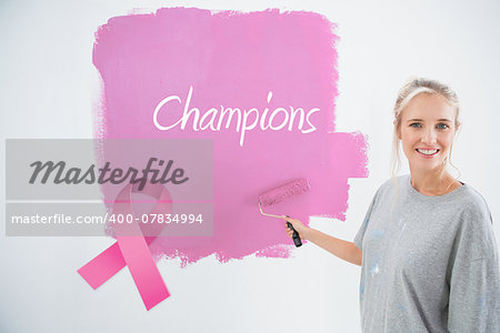 Happy young woman painting her wall pink against pink breast cancer awareness ribbon