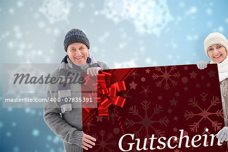 Winter couple showing poster against gift card with festive bow