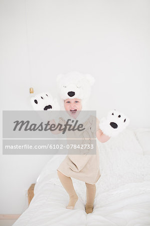 Girl wearing polar bear costume jumping on bed