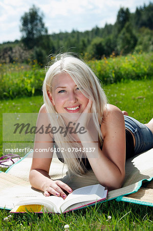 Smiling woman with book lying on grass