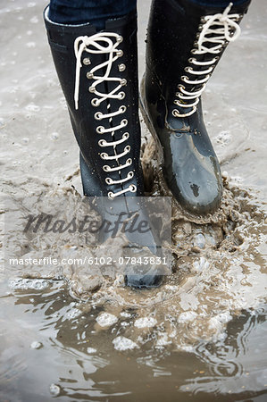 Person in wellington splashing mud, low section