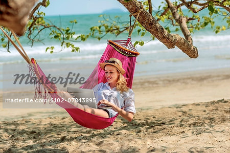 Young woman using laptop in hammock on beach