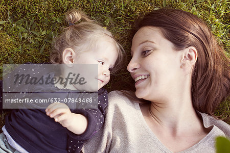 Mother and baby girl lying on grass, smiling at each other