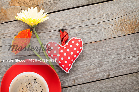 Cup of coffee, heart toy and gerbera flowers on wooden table with copy space