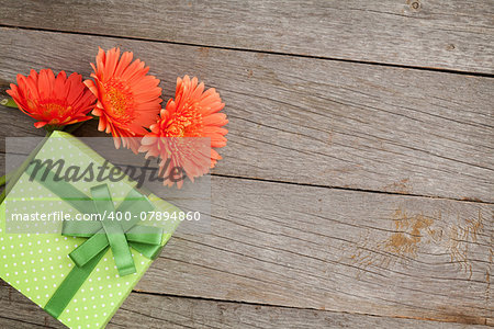 Orange gerbera flowers and gift box on wooden table background with copy space