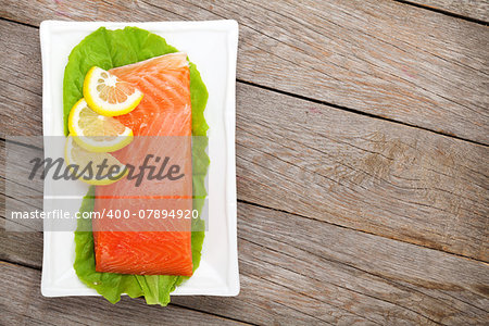 Fresh salmon fish with lemon and salad leaves on wooden table with copy space