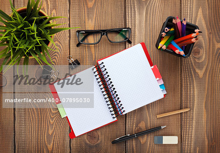Office table with notepad, colorful pencils, supplies and flower. View from above with copy space