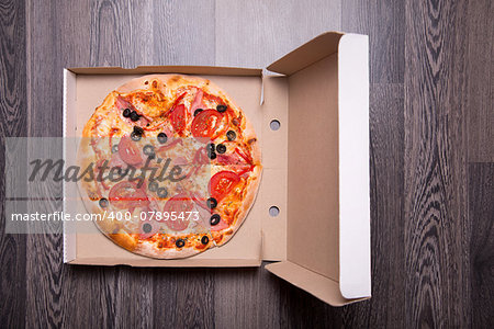 Italian pizza with ham, tomatoes, and olives in box, on gray table background