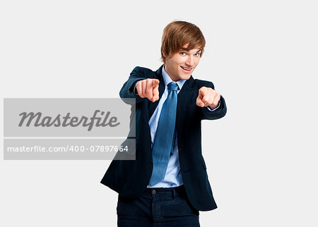 Young businessman looking and pointing to the camera, over a gray background