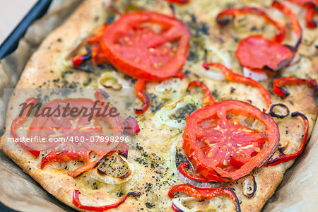 Delicious fresh traditional Italian focaccia bread with tomatoes, red peppers, onions, basil and olive oil on cooking pan