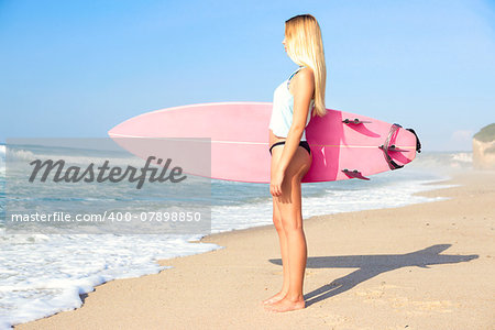 A beautiful surfer girl looking at the beach with her surfboard