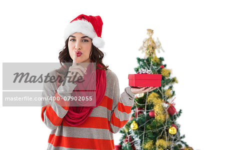 Festive brunette keeping secret and holding gift by the tree on white background