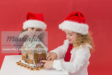 Festive little girls making a gingerbread house on red background