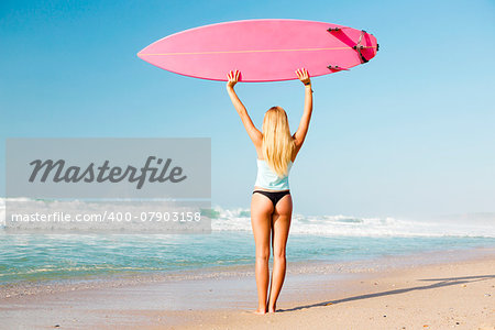 A beautiful surfer girl looking at the beach with her surfboard