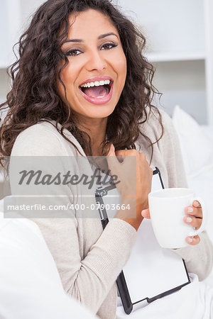 Beautiful young Latina Hispanic woman smiling, laughing, relaxing and drinking a cup of coffee or tea using tablet computer