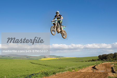 Young male motocross racer jumping mid air over landscape