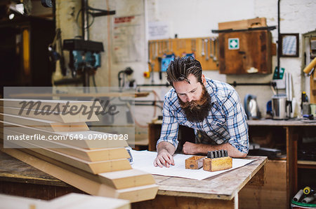 Mid adult craftsman looking down at blueprint in organ workshop