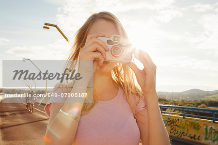 Young woman on bridge taking photographs on digital camera