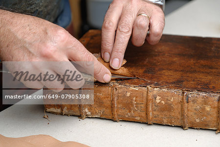 Close up of hands of senior male traditional bookbinder removing leather from book