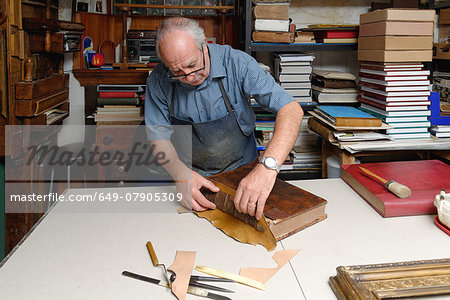 Senior man repairing antique book spine in traditional bookbinding workshop