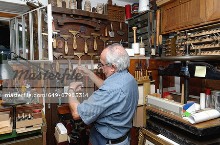 Senior man selecting tools in traditional bookbinding workshop