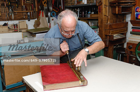 Senior man restoring book in traditional bookbinding workshop
