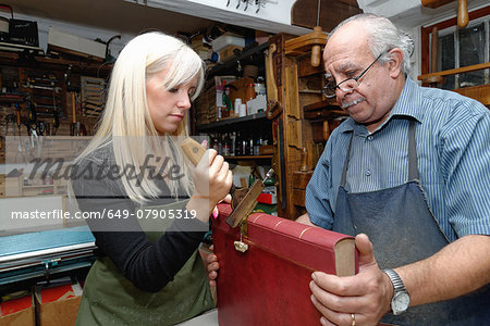Senior man and young woman applying gold leaf to book spine in traditional bookbinding workshop