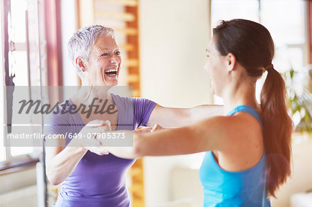 Young female student laughing with teacher in pilates gym
