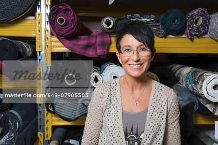 Portrait of mature seamstress in front of rolls of textile in workshop