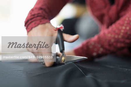 Close up of seamstress hands using scissors to cut textile at work table