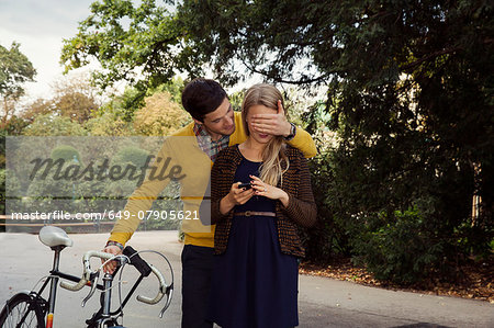 Young man covering girlfriends eyes in park