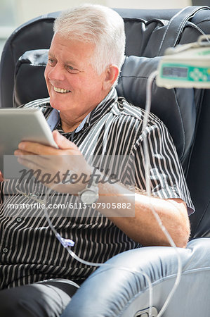 Senior man using tablet pc while receiving intravenous infusion